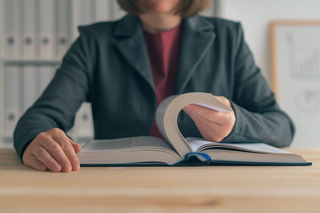 Person at desk with large textbook reading account regulations