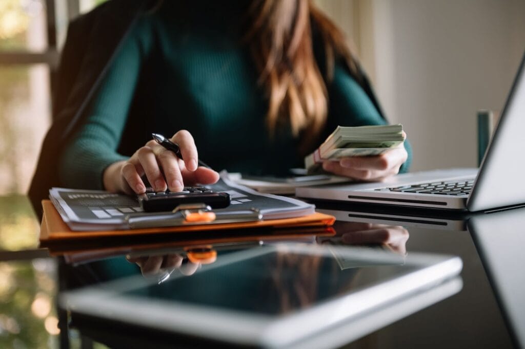 Woman at desk with laptop, cash and calculator